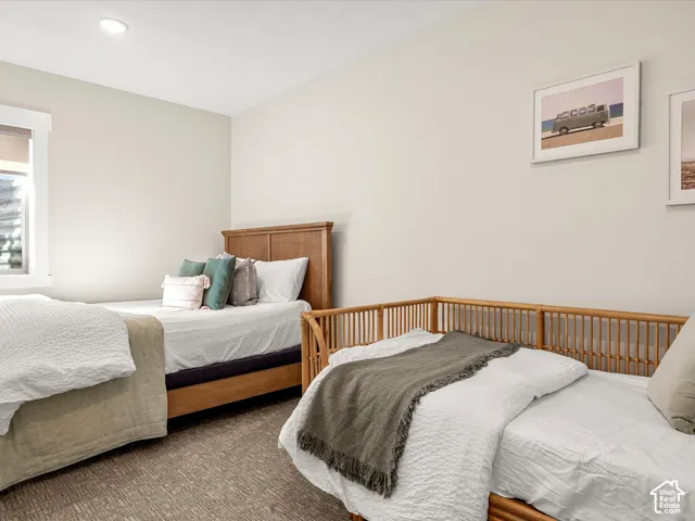 Recessed lighting, window with white trim, light-colored walls, patterned carpeting, and wood-finish bed frames