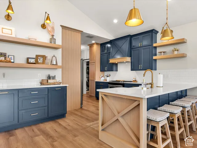Vaulted ceiling, wood-finish flooring, white subway tile backsplash, blue cabinetry, and gold-tone fixtures
