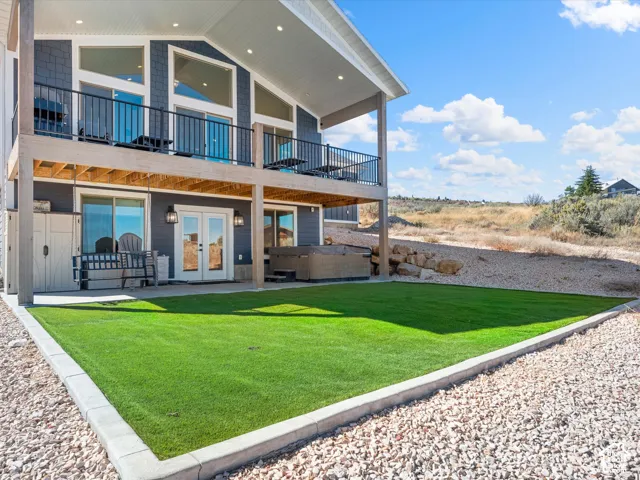 Two-story residence with a gray horizontal siding exterior, a lower-level patio, an upper-level balcony with black railing, and a landscaped yard featuring artificial turf and gravel