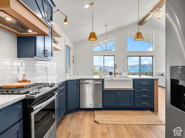 Vaulted ceiling kitchen with integrated stainless steel appliances, wood-finish flooring, white subway tile backsplash, deep blue cabinetry, and a white farmhouse sink
