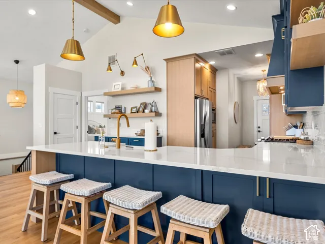 Kitchen featuring a vaulted ceiling, wood-finish flooring, white countertops, blue cabinetry, and brass fixtures