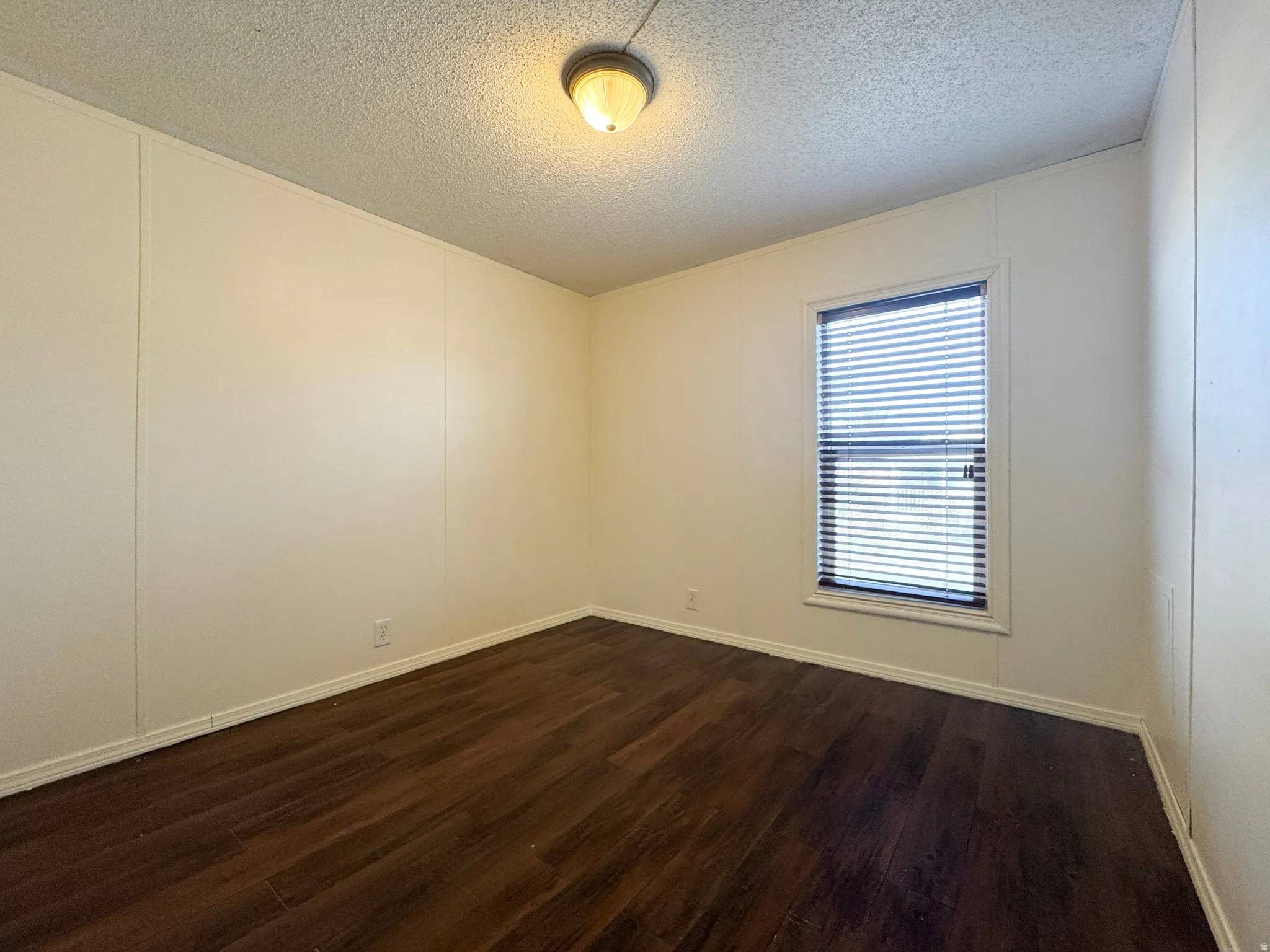 Empty room with a decorative wall, a textured ceiling, and dark wood-style floors