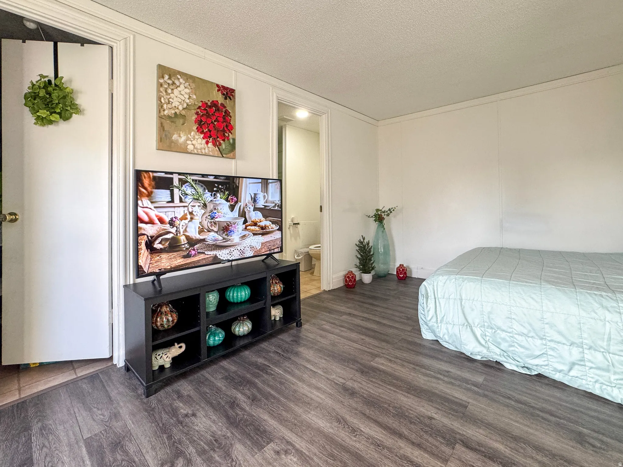 Bedroom with dark wood-type flooring, a decorative wall, a textured ceiling, ensuite bath, and ornamental molding