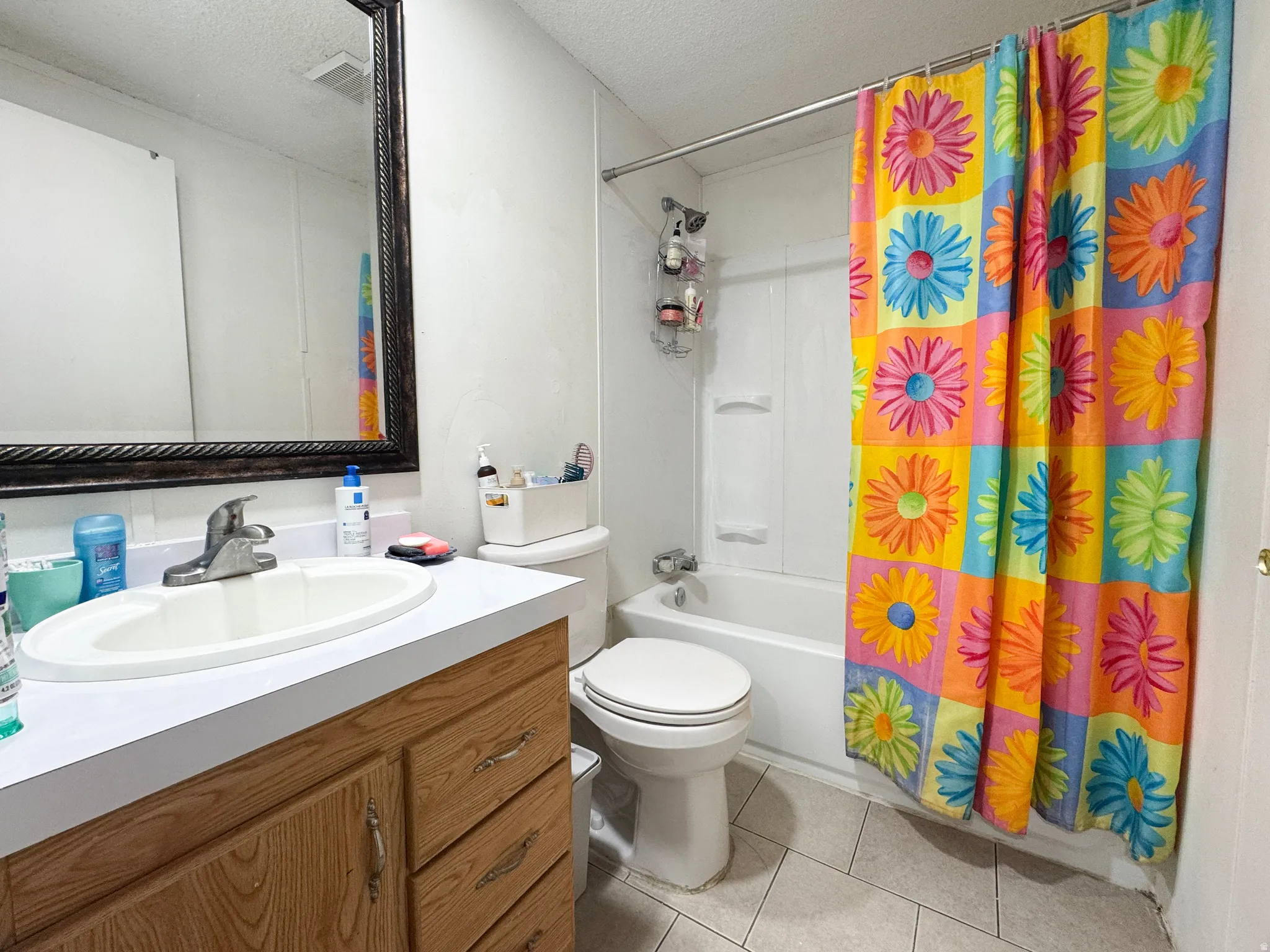 Full bathroom with a textured ceiling, shower / bath combo with shower curtain, vanity, and light tile patterned floors