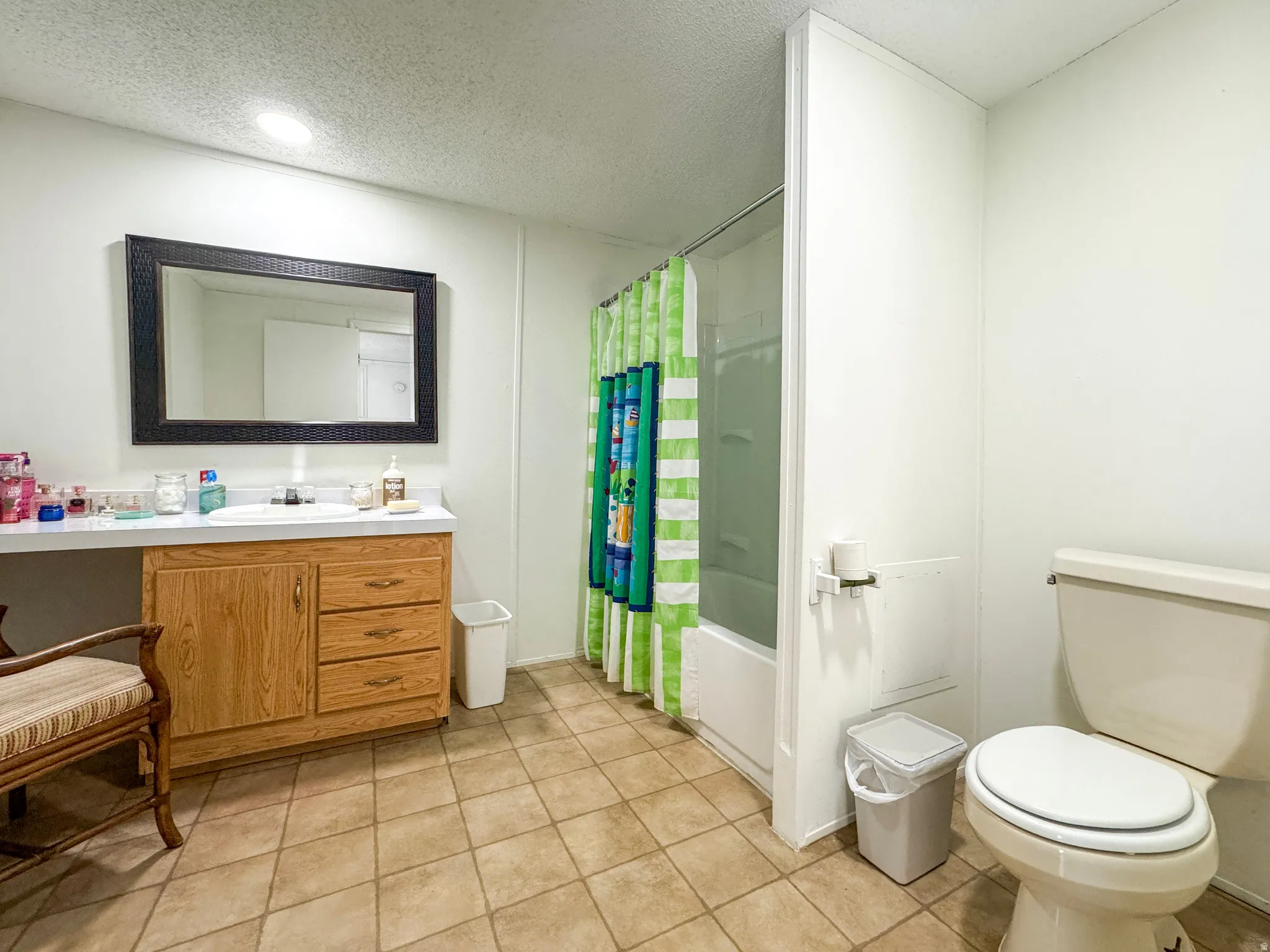 Full bath with vanity, a textured ceiling, shower / bath combo with shower curtain, and light tile patterned flooring