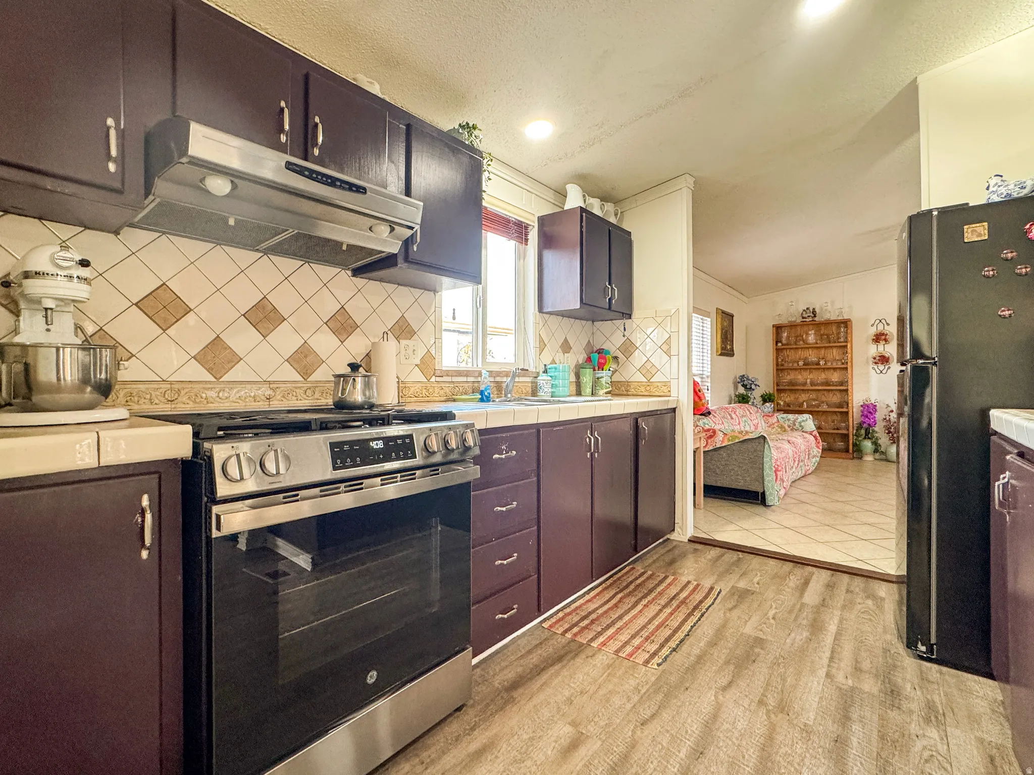 Kitchen featuring stainless steel range with gas cooktop, tile countertops, freestanding refrigerator, light wood-style flooring, and tasteful backsplash