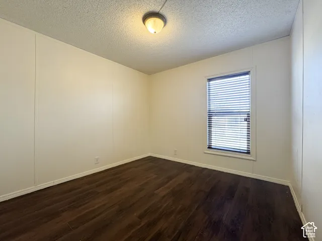 Empty room with a decorative wall, a textured ceiling, and dark wood-style floors
