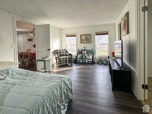Bedroom with dark wood-style flooring, a decorative wall, a textured ceiling, and crown molding