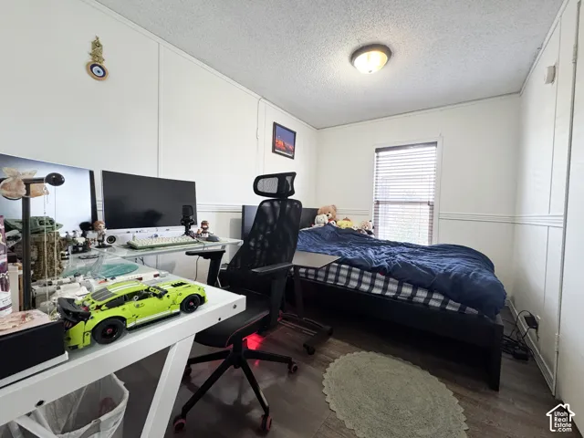 Bedroom featuring a textured ceiling, dark wood-style flooring, a desk, and a decorative wall