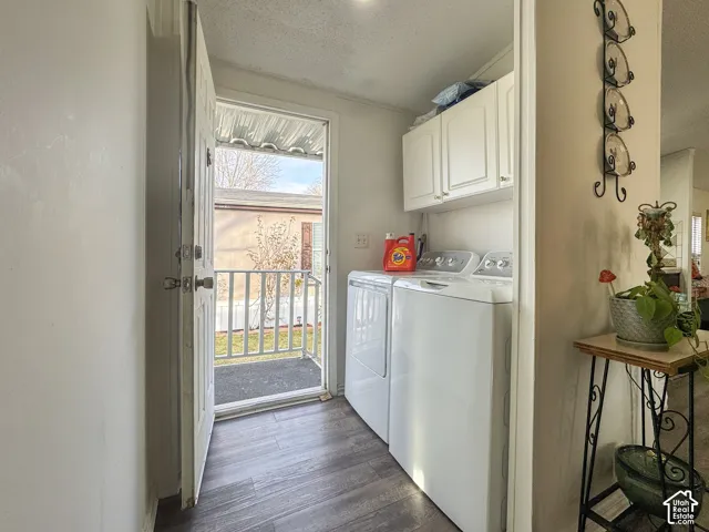 Laundry area with cabinet space, a textured ceiling, washer and clothes dryer, and dark wood-type flooring