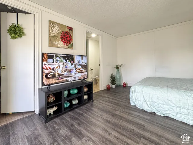Bedroom with dark wood-type flooring, a decorative wall, a textured ceiling, ensuite bath, and ornamental molding
