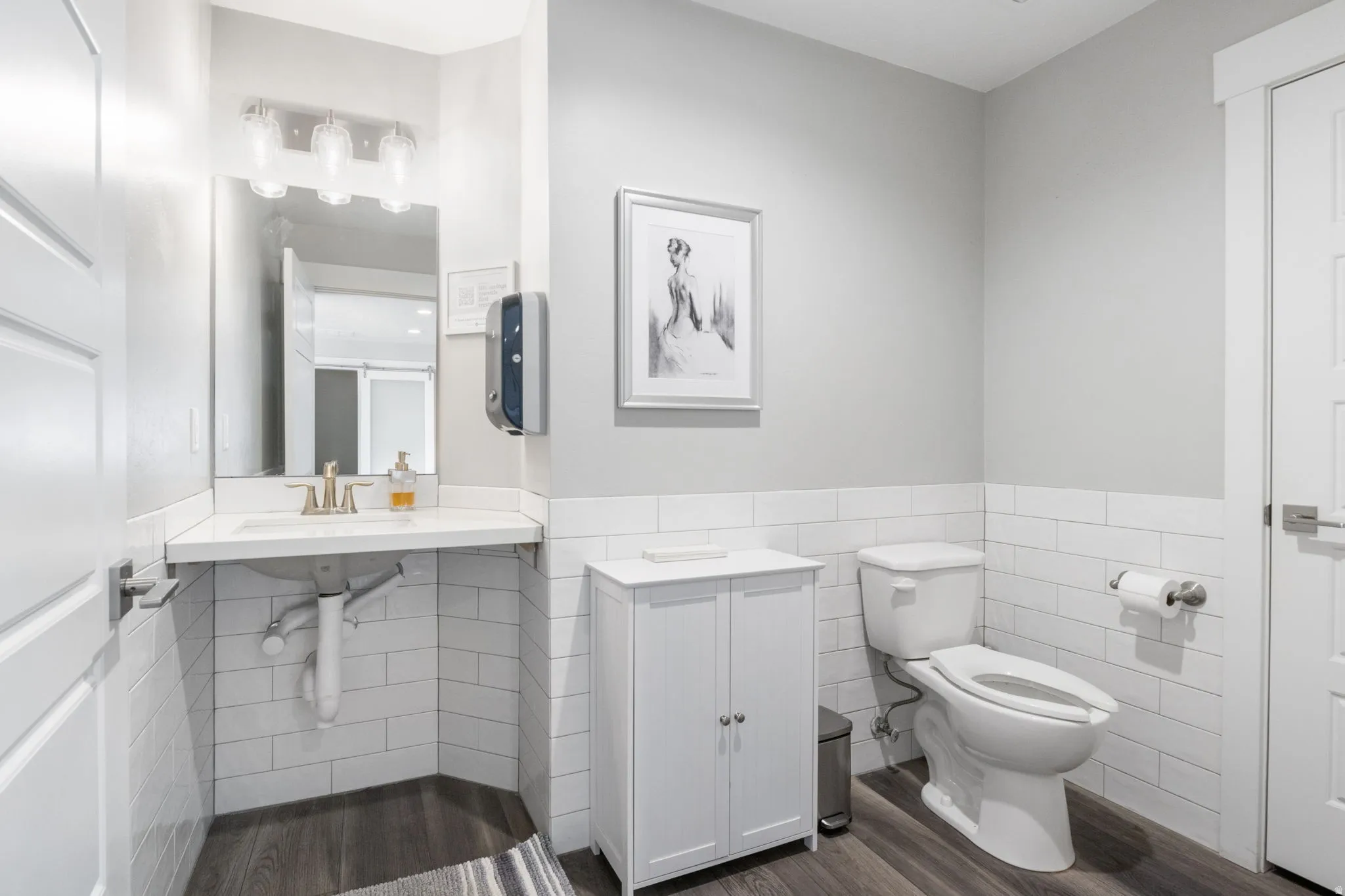Half bathroom featuring tile walls, a wainscoted wall, and dark wood finished floors