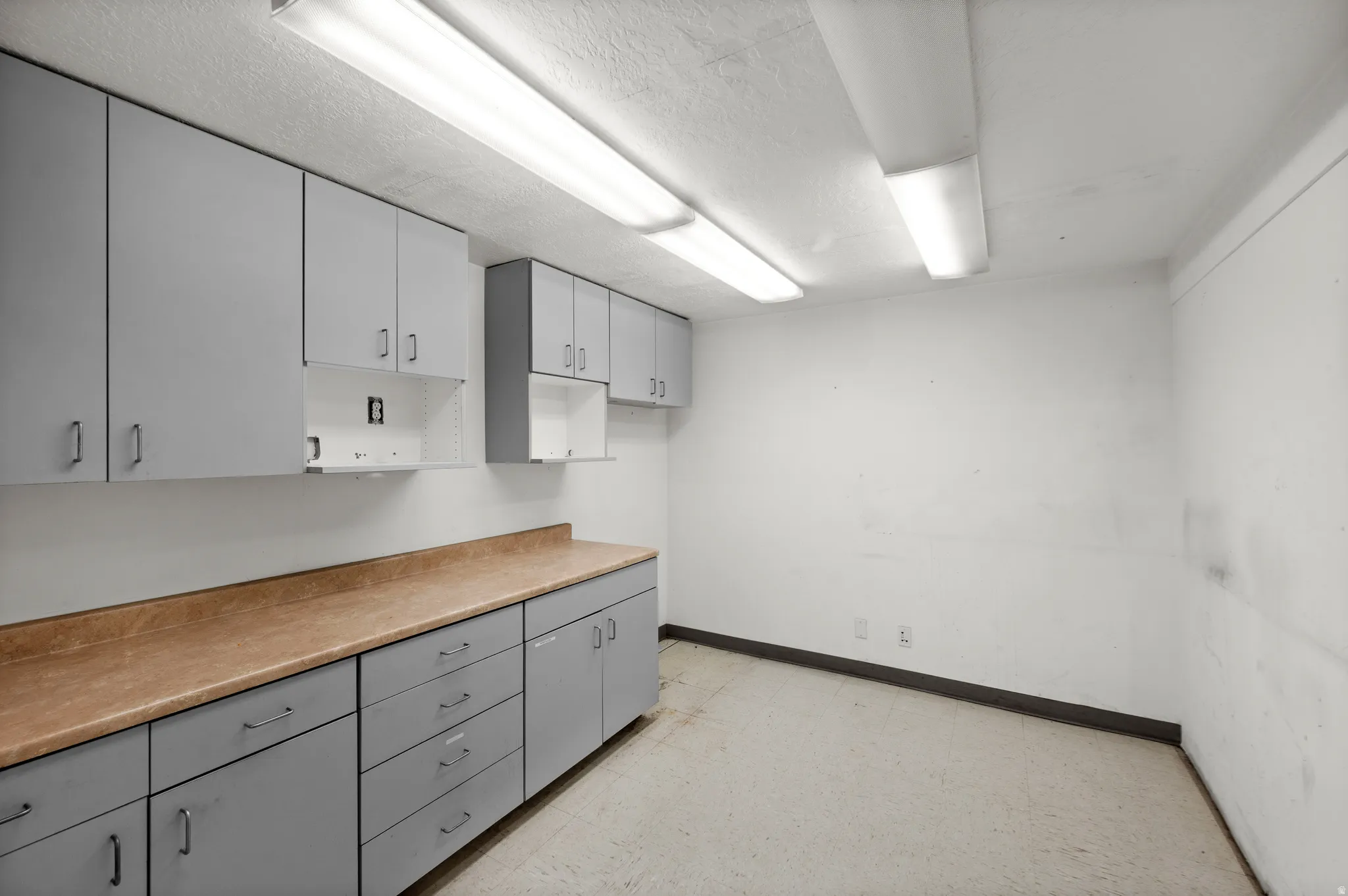 Kitchen with light flooring, two tone cabinetry, light countertops, and a textured ceiling