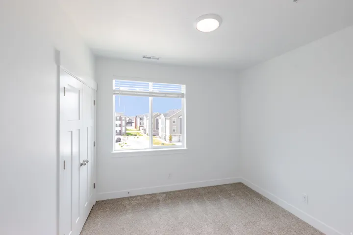 Neutral paint scheme, carpeted flooring, window with blinds, flush mount ceiling light, and panel doors with silver-tone hardware