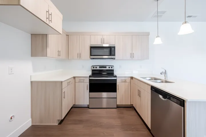 U-shaped kitchen with wood-finish cabinetry, light-toned countertops, and stainless steel appliances