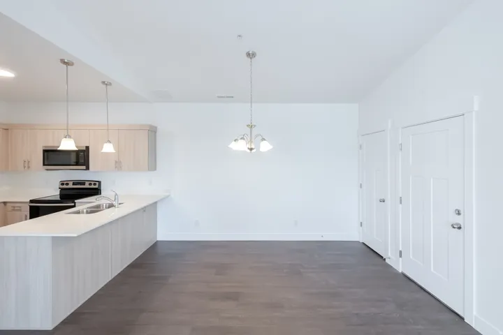Open-concept living space with dark wood-finish flooring, white walls, light wood-finish cabinetry, and stainless steel appliances