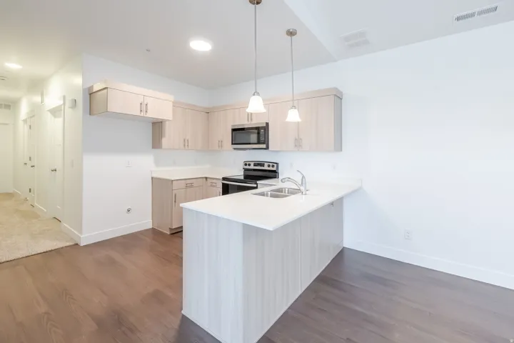 Open-concept kitchen featuring light-toned cabinetry, stainless steel appliances, a breakfast bar, recessed lighting, and wood-finish flooring