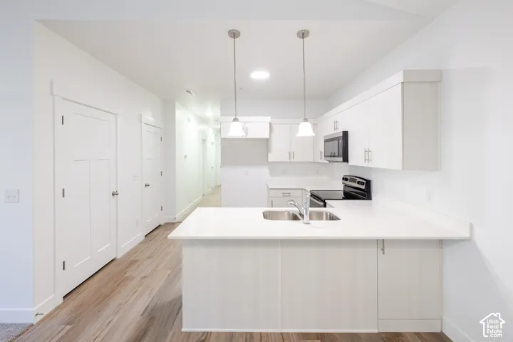 Kitchen featuring white shaker-style cabinetry, solid-surface countertops, wood-finish flooring, a stainless steel dual-basin undermount sink, and dual pendant lighting