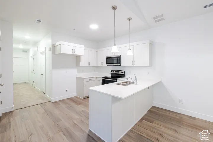 Kitchen featuring white cabinetry, solid surface countertops, a peninsula with a dual-basin sink, integrated stainless steel appliances, and wood-finish flooring