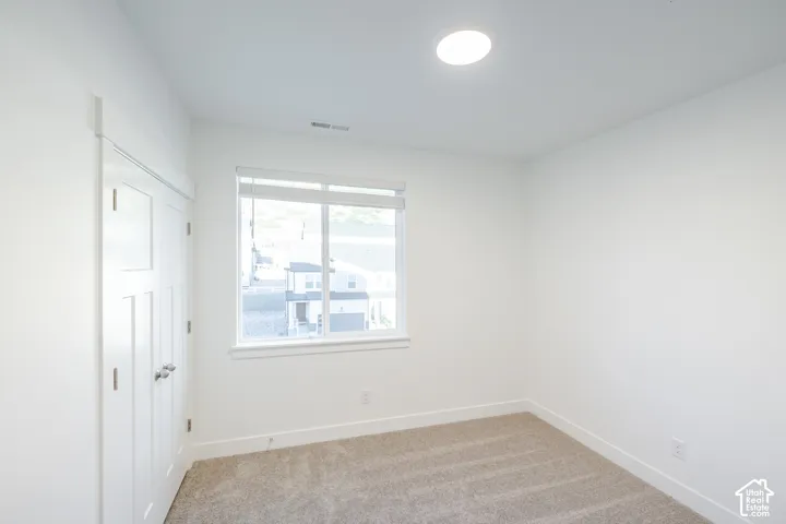 Neutral-toned carpeted flooring, white walls, dual-panel closet doors, and a window with horizontal blinds