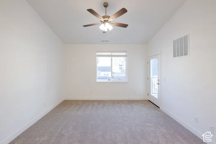 Vaulted ceiling featuring a central five-blade ceiling fan with integrated lighting, wall-to-wall carpeting, and a glass-panel exterior door