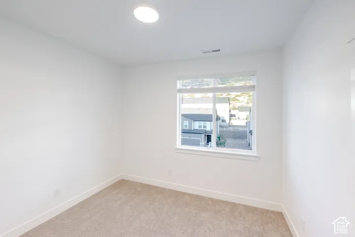 Neutral-toned interior featuring wall-to-wall carpeting, crisp white walls, a single-pane window with integrated blinds, and flush-mount ceiling lighting