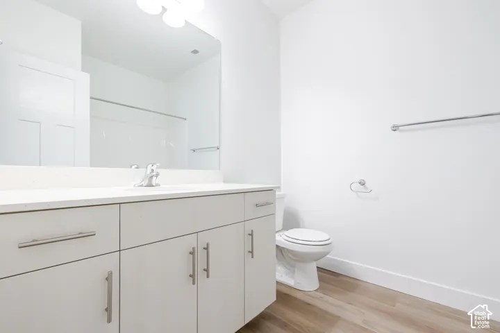 Light-toned cabinetry with satin nickel pulls, stone-surface countertop, integrated vanity sink with chrome faucet, full-width mirror, and wood-finish flooring