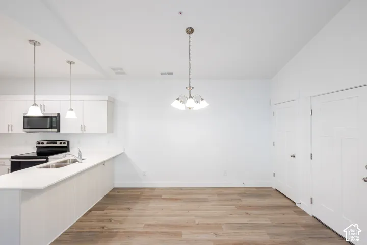 Kitchen featuring white shaker-style cabinetry, solid-surface countertops, wood-finish flooring, a vaulted ceiling, and tiered pendant lighting