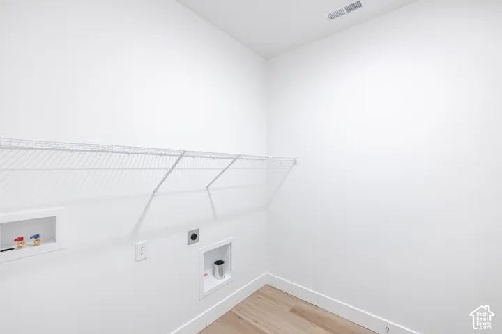 Dedicated laundry space featuring wood-finish flooring, white walls, and a built-in wire shelving system