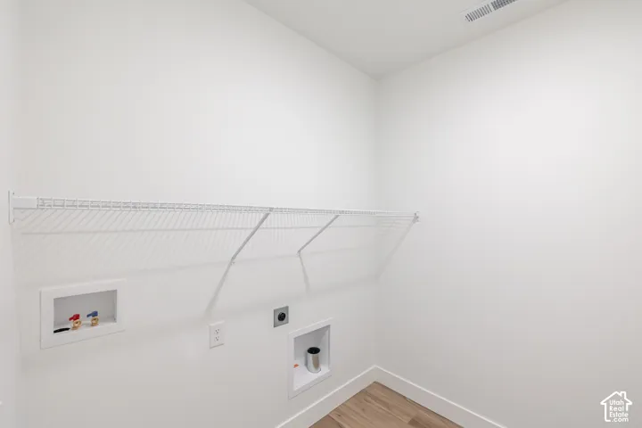 Utility area featuring wood-finish flooring, white walls, and a wall-mounted wire shelving unit