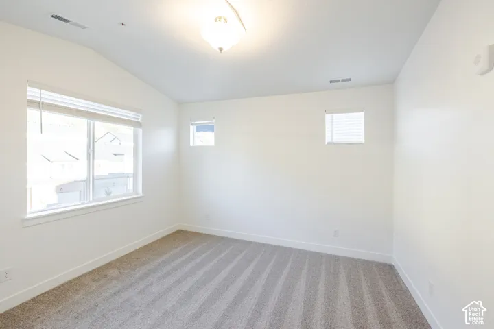 Vaulted ceilings, neutral carpeting, and multi-paned windows featuring integrated blinds and a flush-mount light fixture