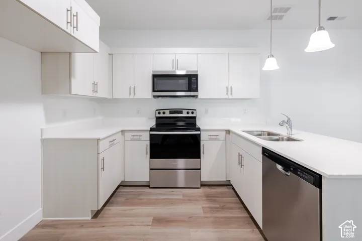 Kitchen featuring white cabinetry, quartz countertops, stainless steel appliances, wood-finish flooring, and dual pendant lighting