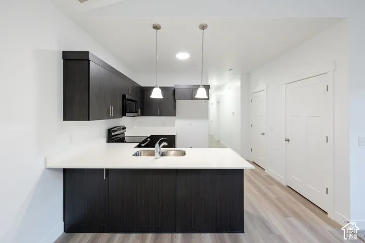 Kitchen featuring dark-toned cabinetry, solid-surface countertops, dual-basin undermount sink, pendant lighting, and wood-finish flooring