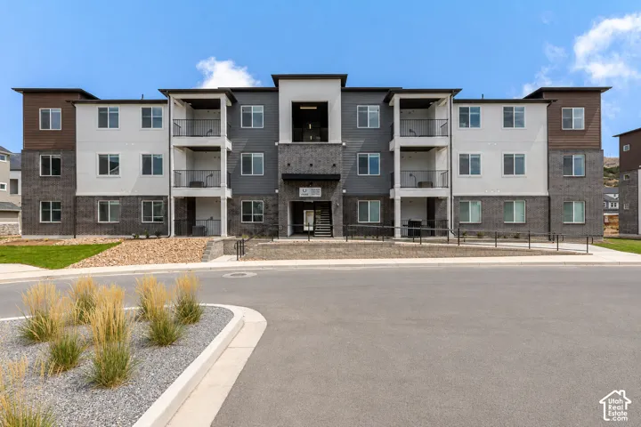 Multi-story residential exterior featuring a mixed-material facade of stone veneer, stucco, and wood-finish siding, complemented by private balconies and paved ground-level entry