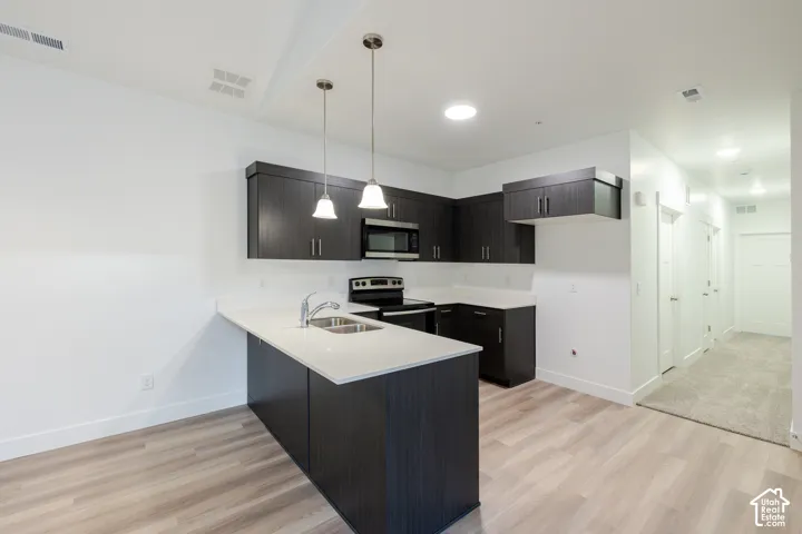 Kitchen featuring dark wood-finish cabinetry, quartz countertops, stainless steel appliances, dual pendant lighting, and wood-finish flooring