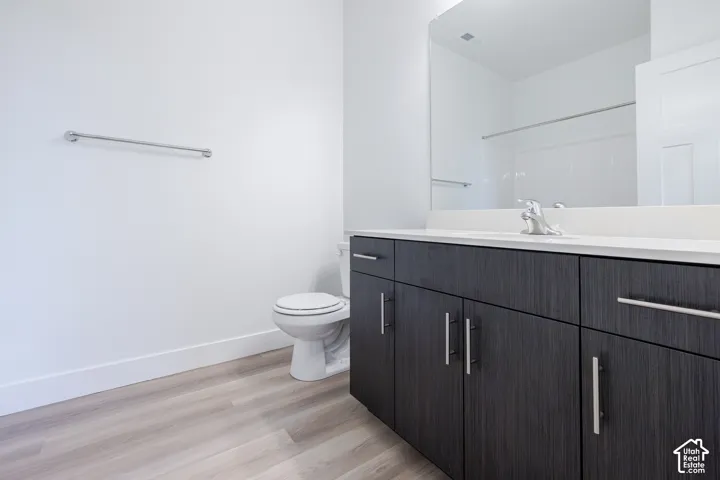 Bathroom featuring dark-toned cabinetry with modern hardware, a countertop basin with a polished chrome faucet, a large wall-mounted mirror, and wood-finish flooring
