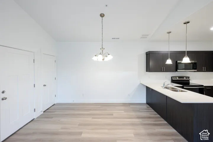 Kitchen featuring dark wood-finish cabinetry, solid-surface countertops, stainless steel appliances, wood-finish flooring, and multi-light pendant fixtures