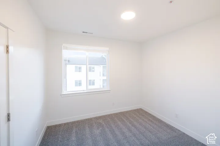 Neutral-toned carpeted flooring, white wall finishes, sliding window with horizontal blinds, and a circular flush-mount ceiling light