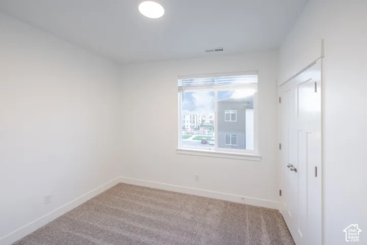 Neutral-toned carpeting, high-ceiling design, dual-panel closet doors with metallic hardware, and a single-hung window with integrated blinds