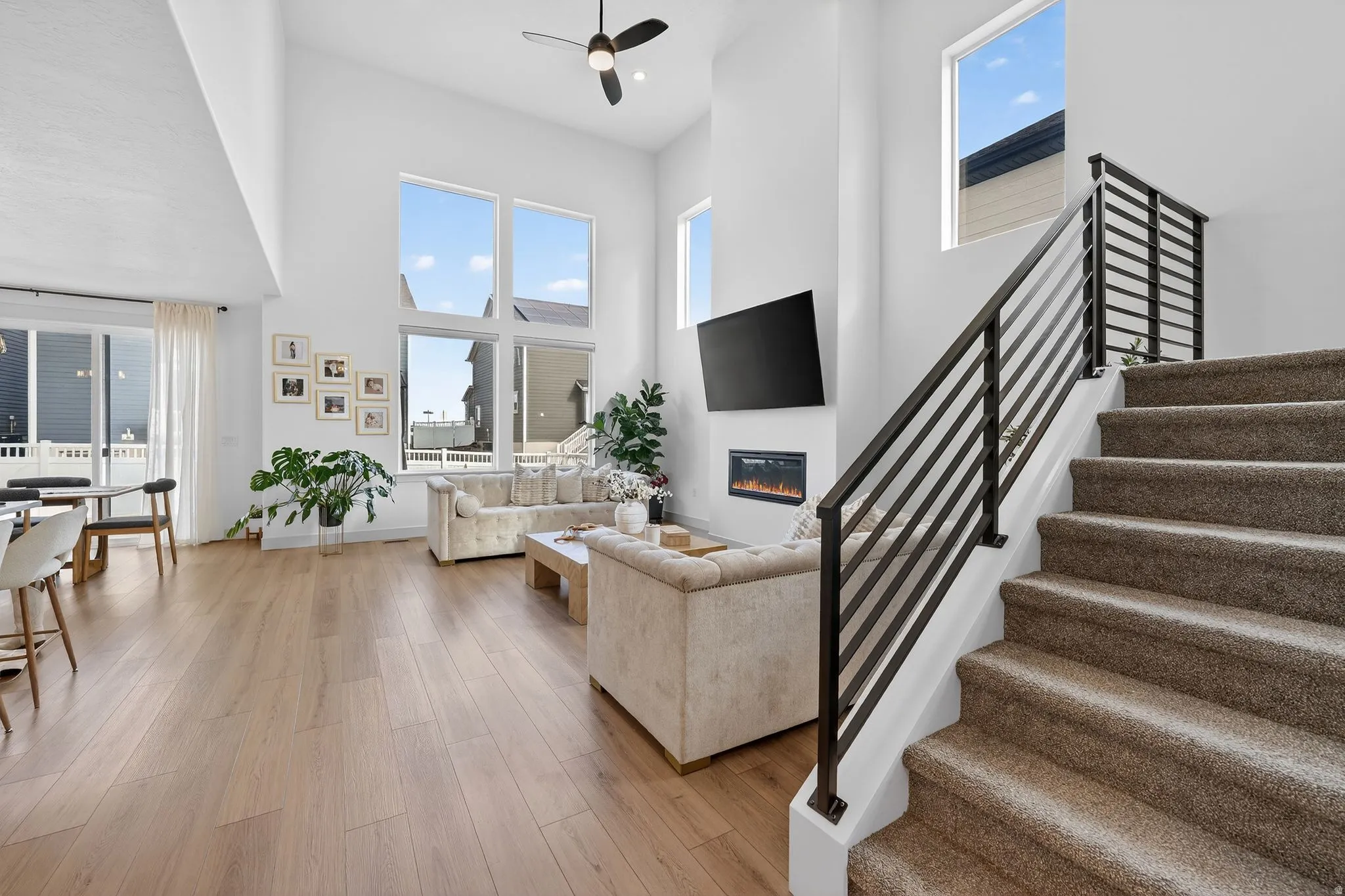 Living room with light wood-style floors, a ceiling fan, a high ceiling, and a glass covered fireplace