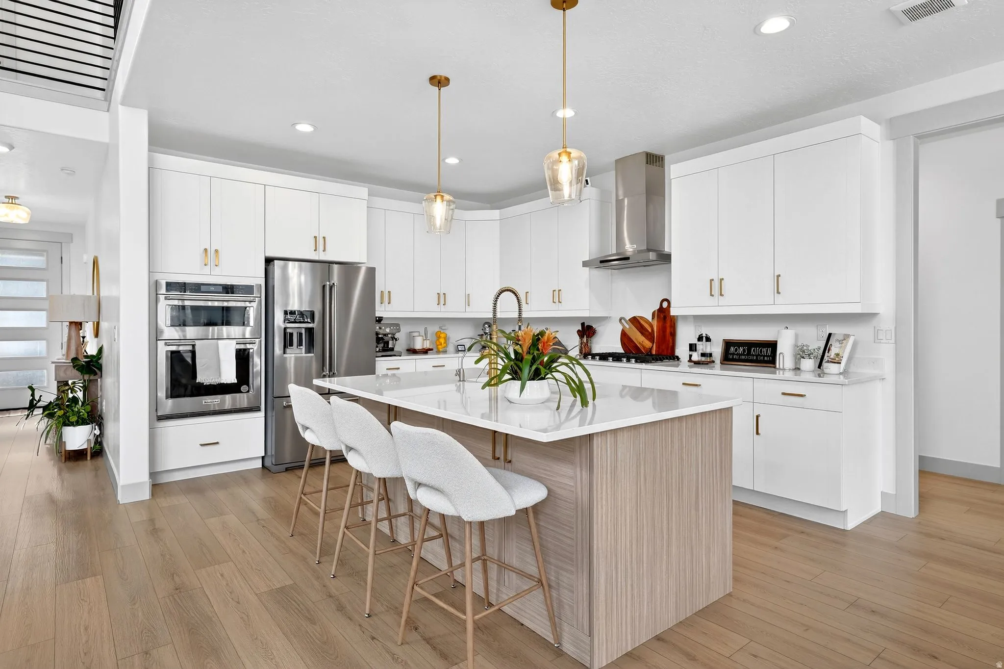 Two tone kitchen with stainless steel appliances, decorative light fixtures, a kitchen island with sink, a breakfast bar, and light wood-style flooring