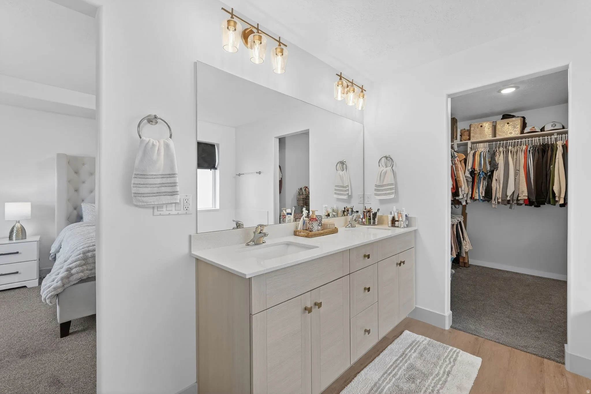 Full bathroom with a spacious closet, double vanity, ensuite bathroom, and light carpet