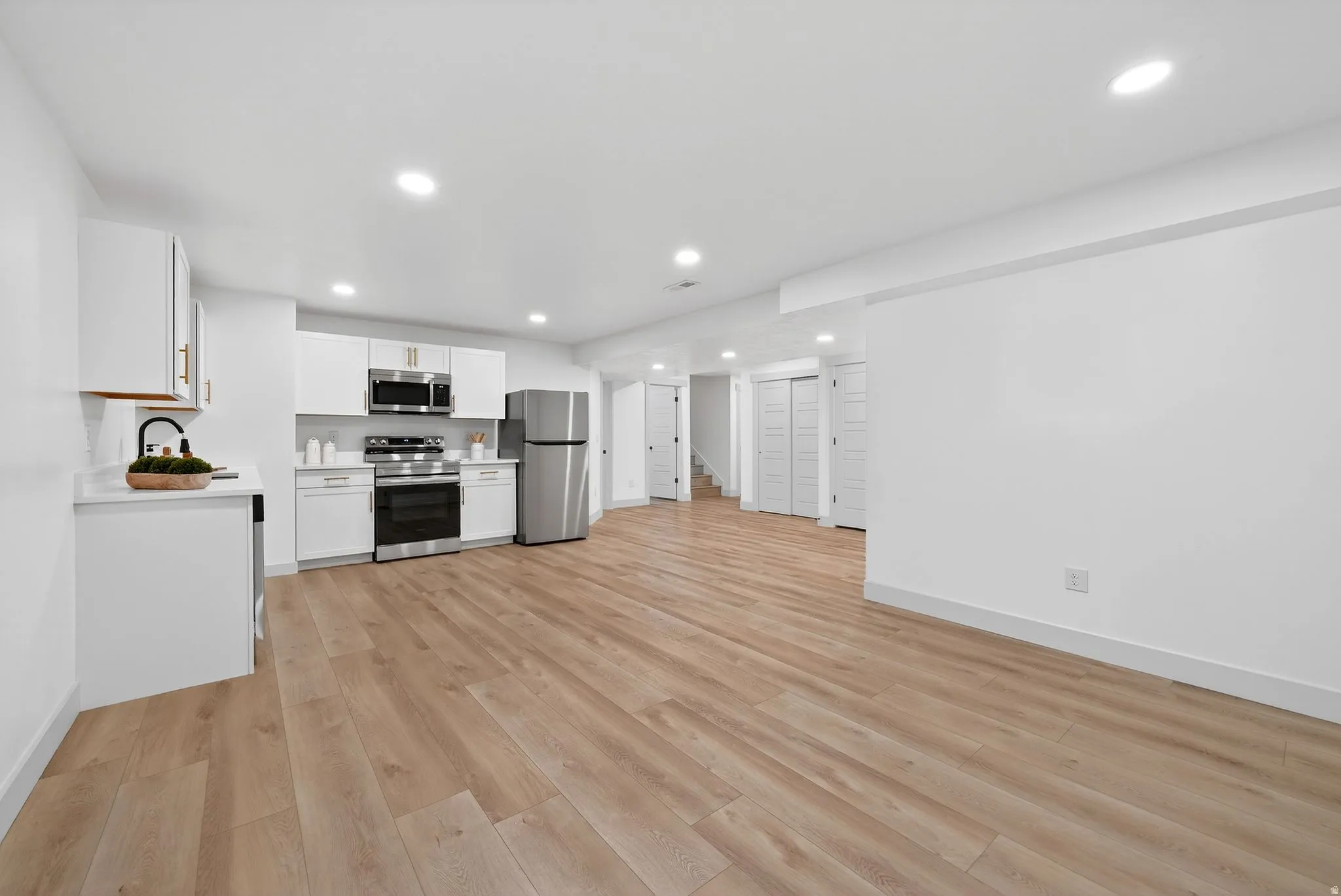 Kitchen with light countertops, white cabinets, stainless steel appliances, light wood-style flooring, and recessed lighting