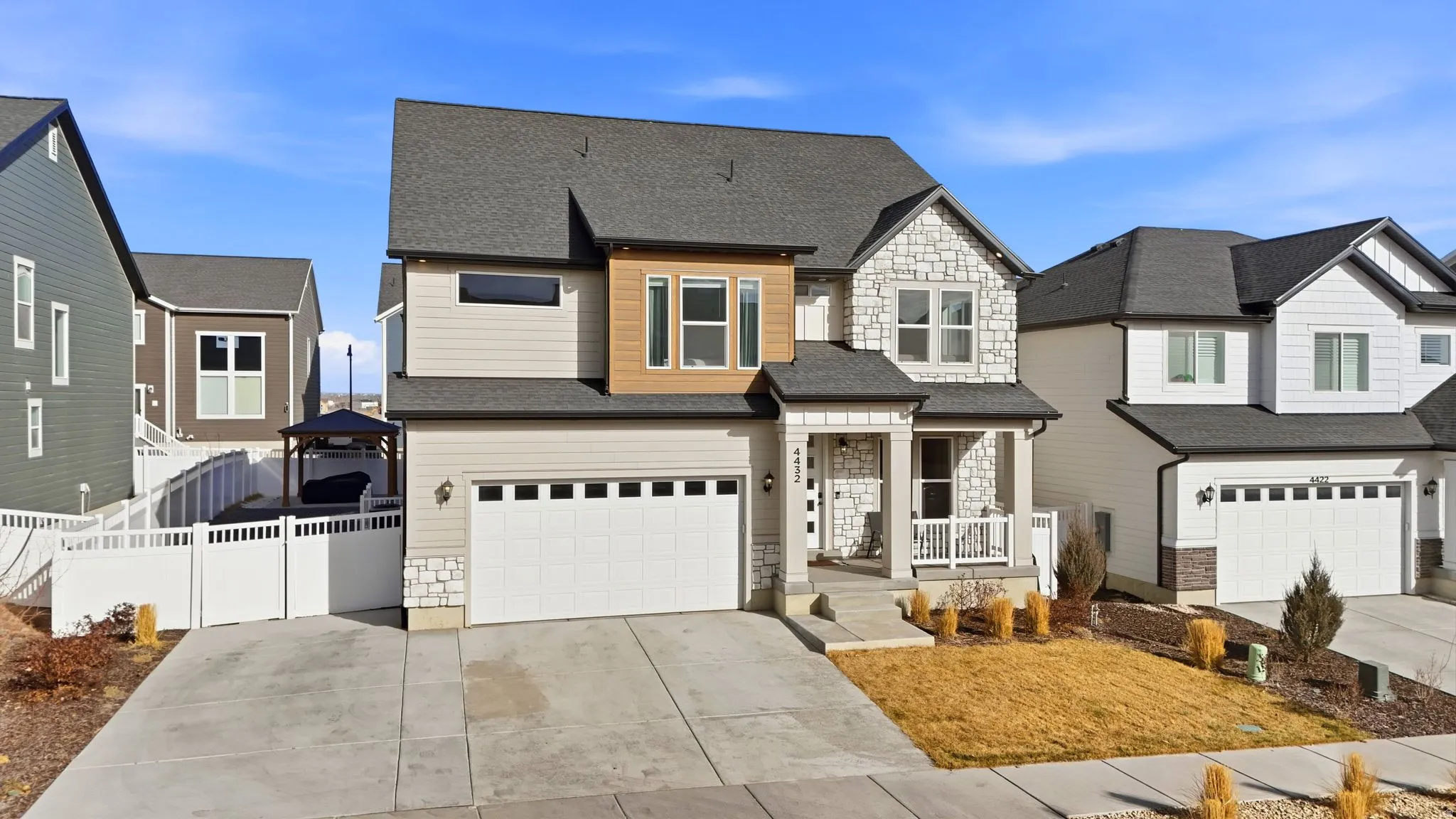 View of front of house with stone siding, driveway, roof with shingles, an attached garage, and a gazebo