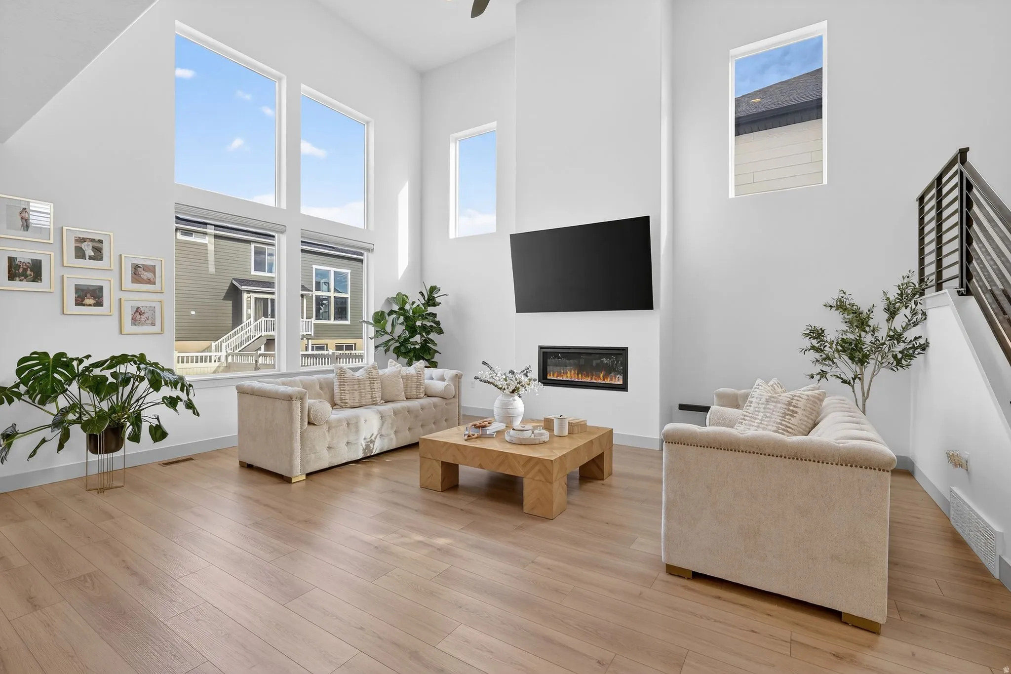 Living area with a high ceiling, light wood-style floors, plenty of natural light, ceiling fan, and a glass covered fireplace