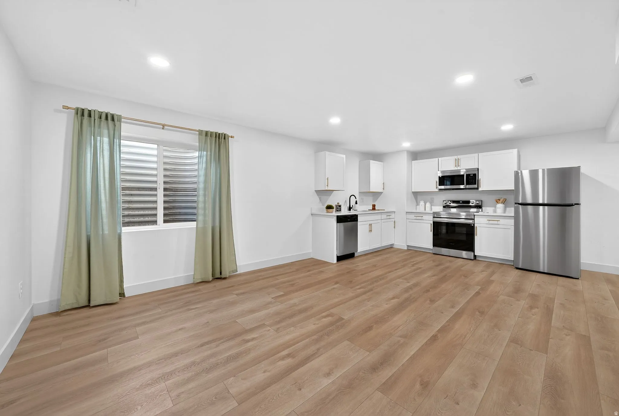 Kitchen featuring stainless steel appliances, light countertops, white cabinetry, light wood-type flooring, and recessed lighting
