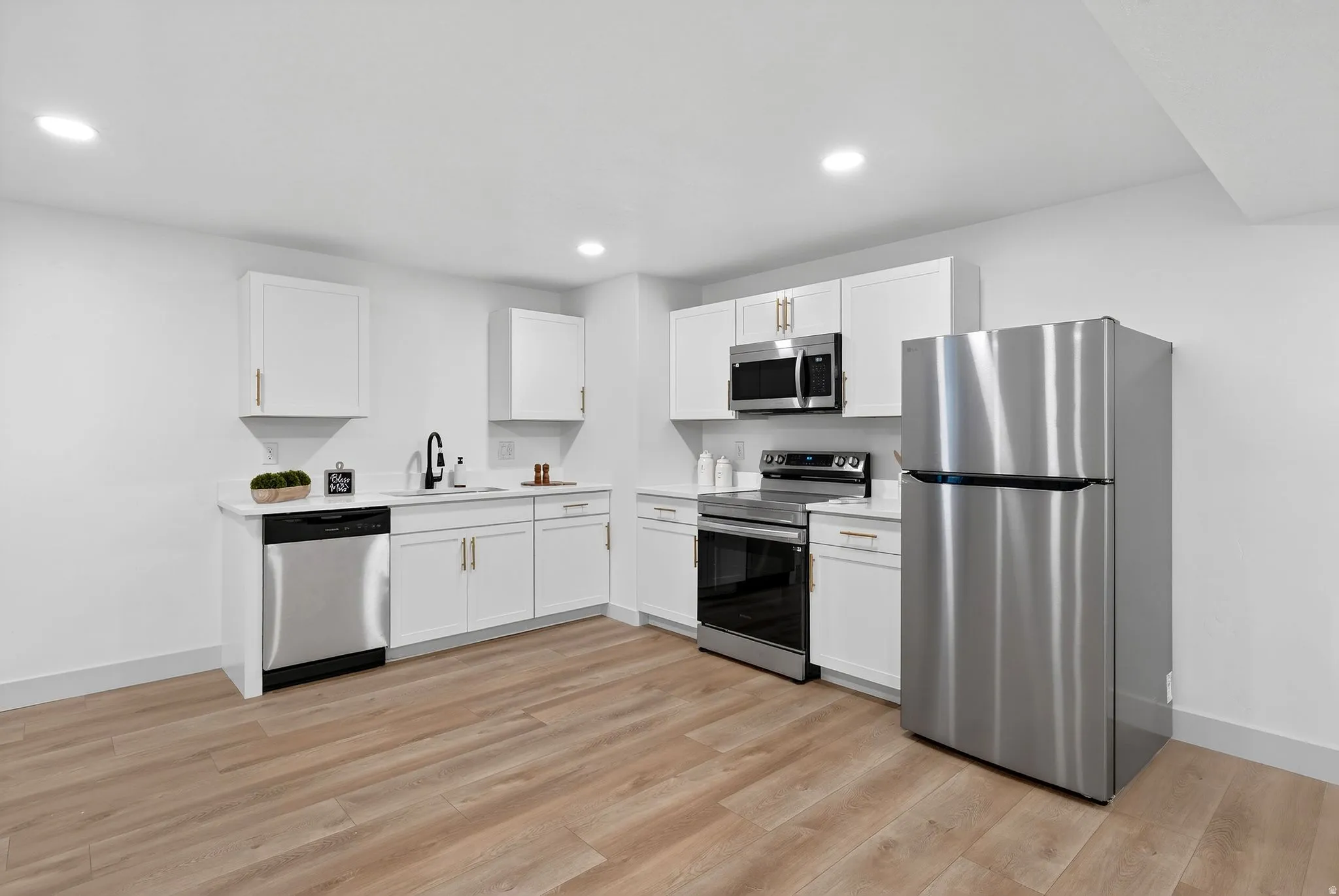 Kitchen with stainless steel appliances, white cabinetry, light wood finished floors, and recessed lighting