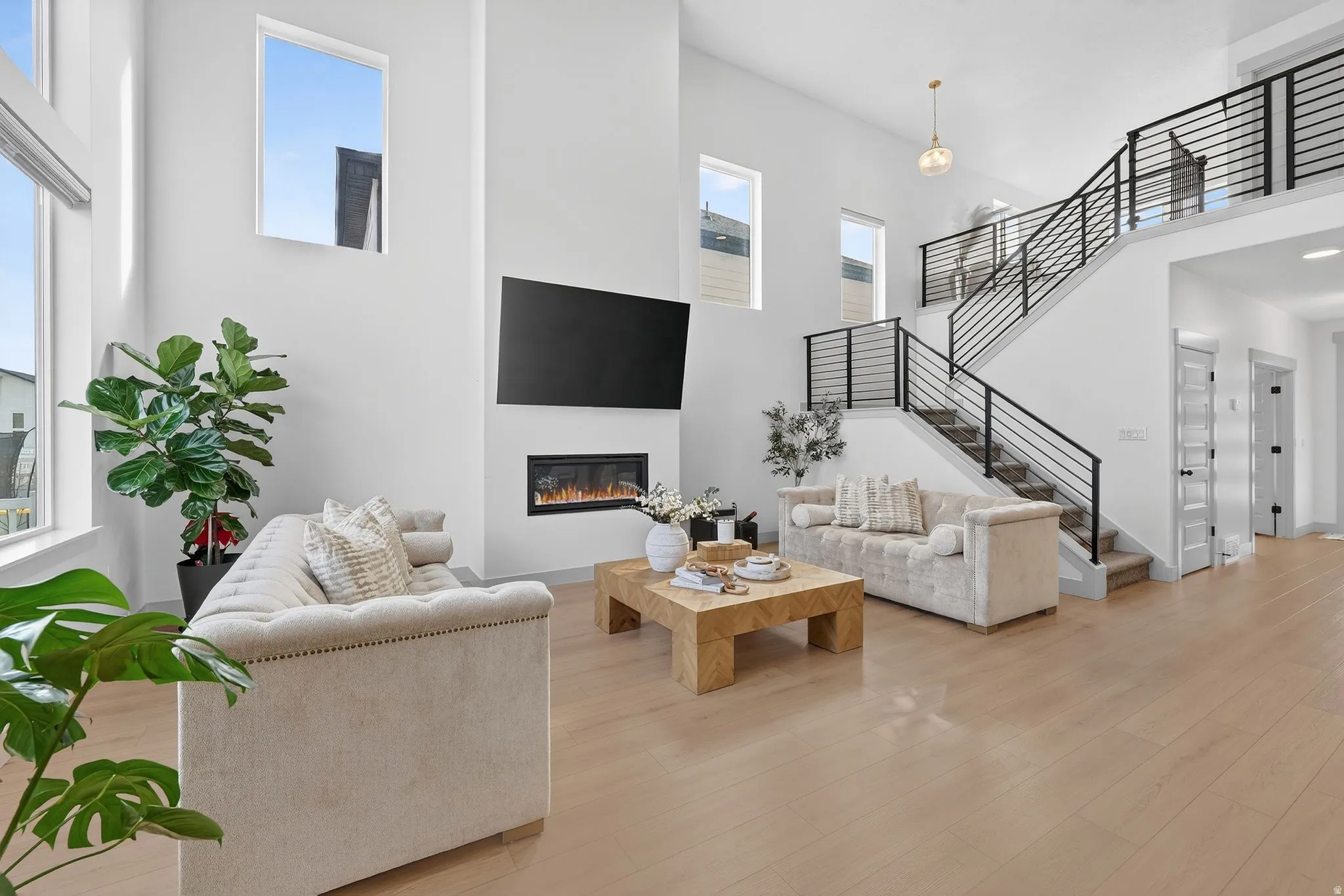 Living room with a high ceiling, light wood-style floors, and a glass covered fireplace