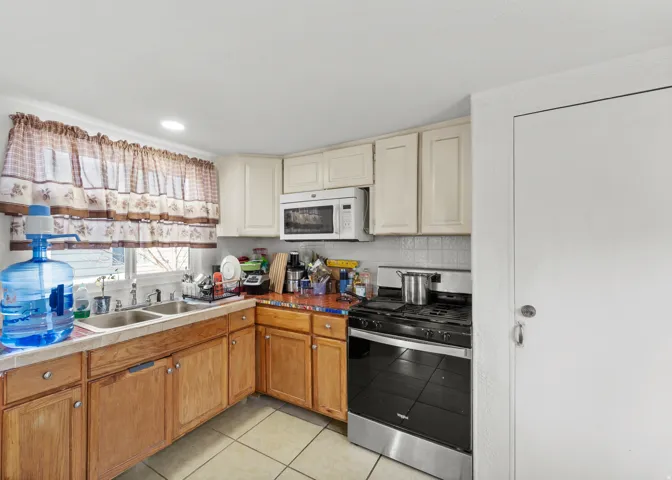 Kitchen with gas stove, white microwave, light tile patterned floors, recessed lighting, and cream cabinetry