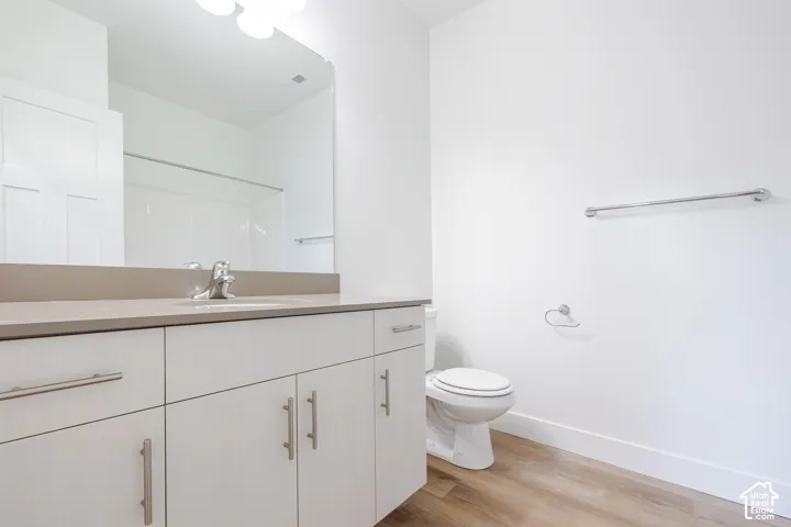 Bathroom featuring light-toned cabinetry with metal hardware, smooth solid-surface countertop with an integrated sink, large wall-mounted mirror, and wood-finish flooring